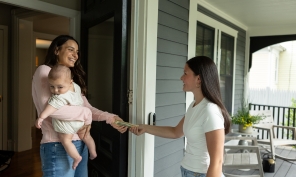 Mom with baby in her arms paying a teenager money for babysitting.