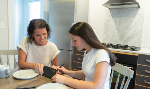 A mom helping her daughter balance her checkbook at the kitchen table.