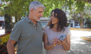 Middled aged couple on a walk and talking about what the woman is showing on her phone.