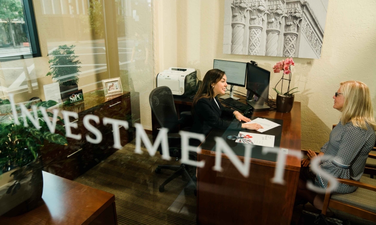 Financial Advisor meeting with a customer behind a glass door with the word Investments.