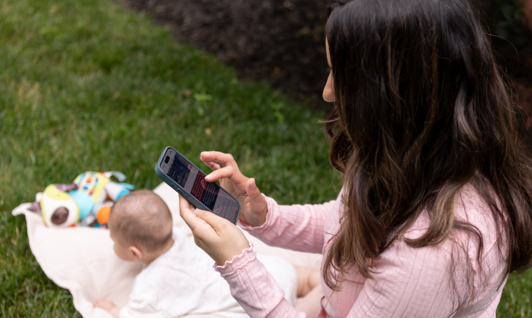 Young mom checking her WSB bank account on her mobile app while baby is doing tummy time.