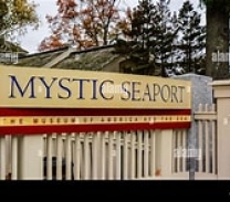 Large yellow sign on a fence displaying the name Mystic Seaport