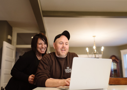 Couple smiling and looking at a laptop.