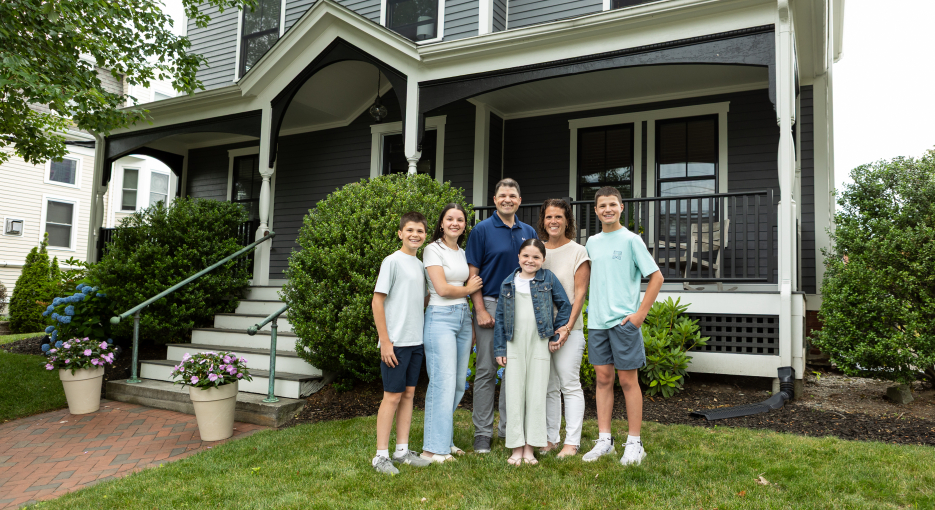 Family of six standing in the front yard of a colonial home.