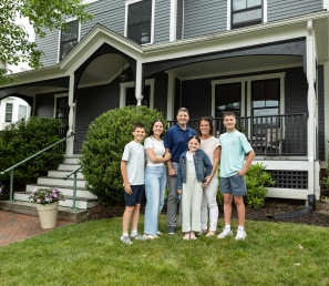 Family of six standing in the front yard of a colonial home.