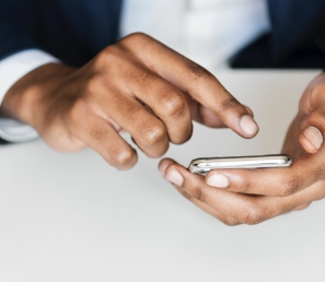 Hand shown holding a phone with the other tapping on the phone held by a person in a business suit.
